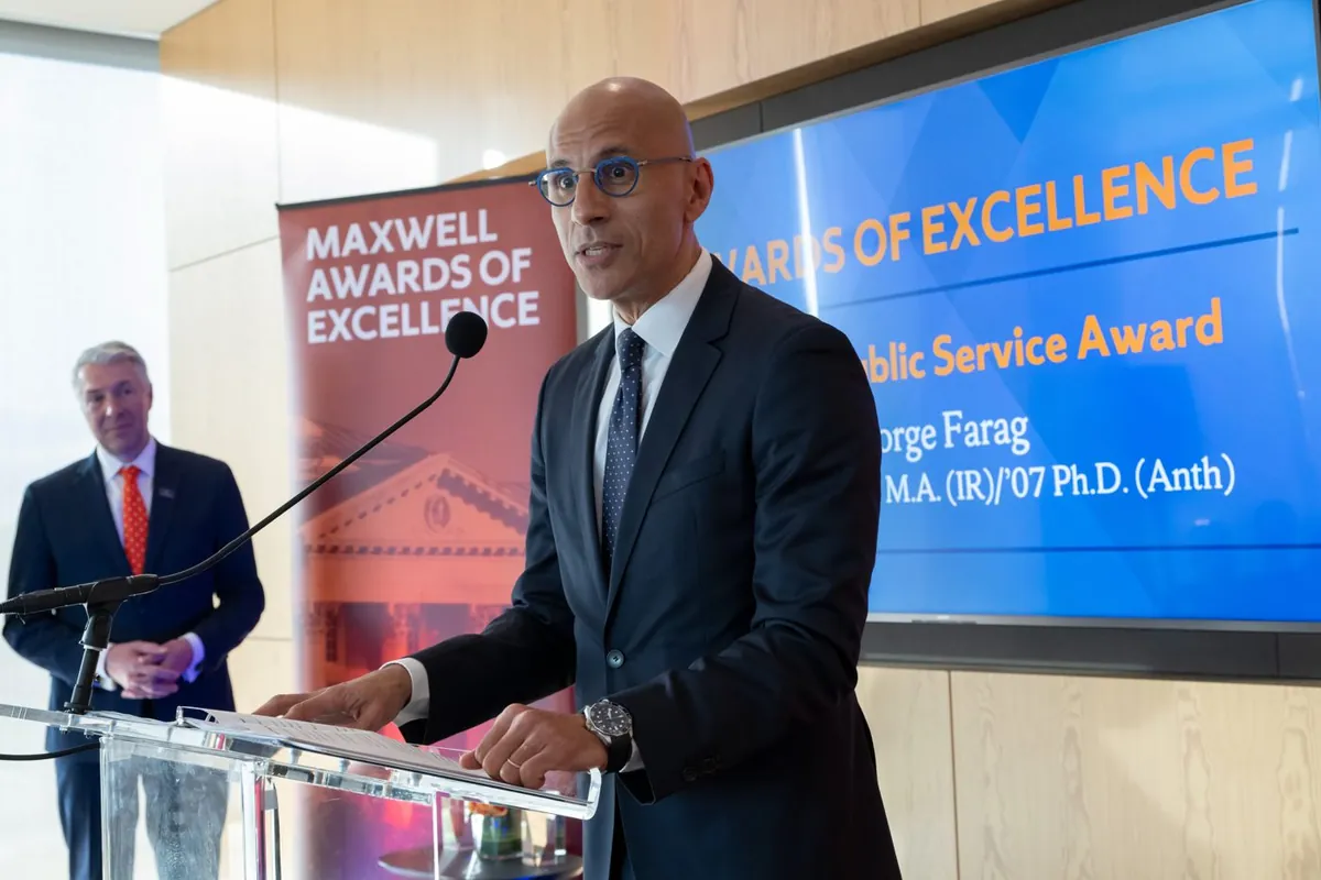 George Farag speaking at a podium at the Maxwell Awards of Excellence, with Public Service Award on the screen behind him